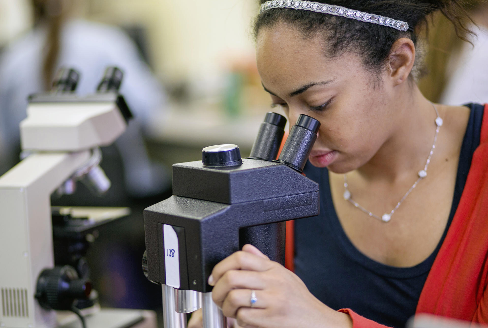 A young woman looks through a microscope.