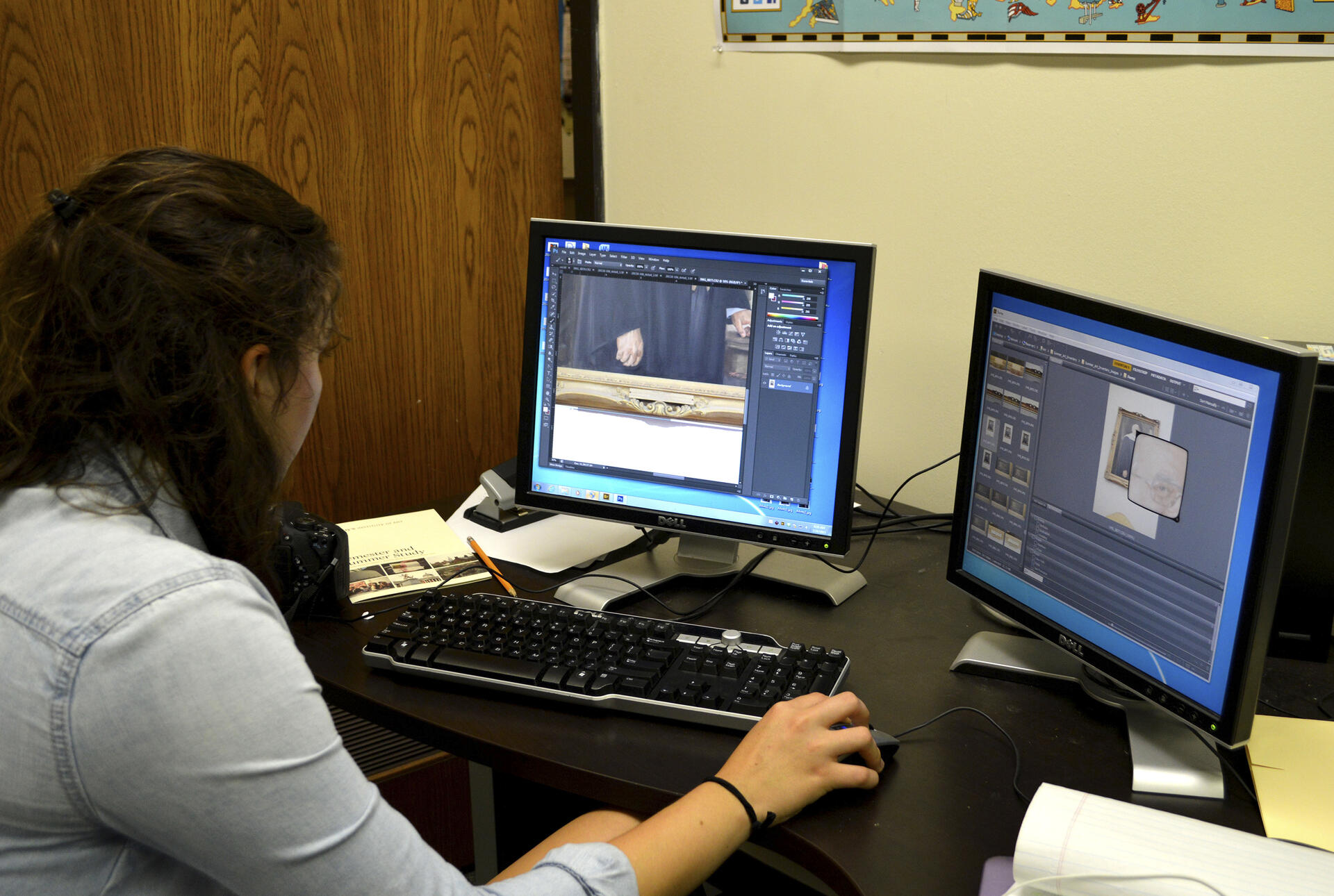 A dark haired young woman works at a computer with two screens