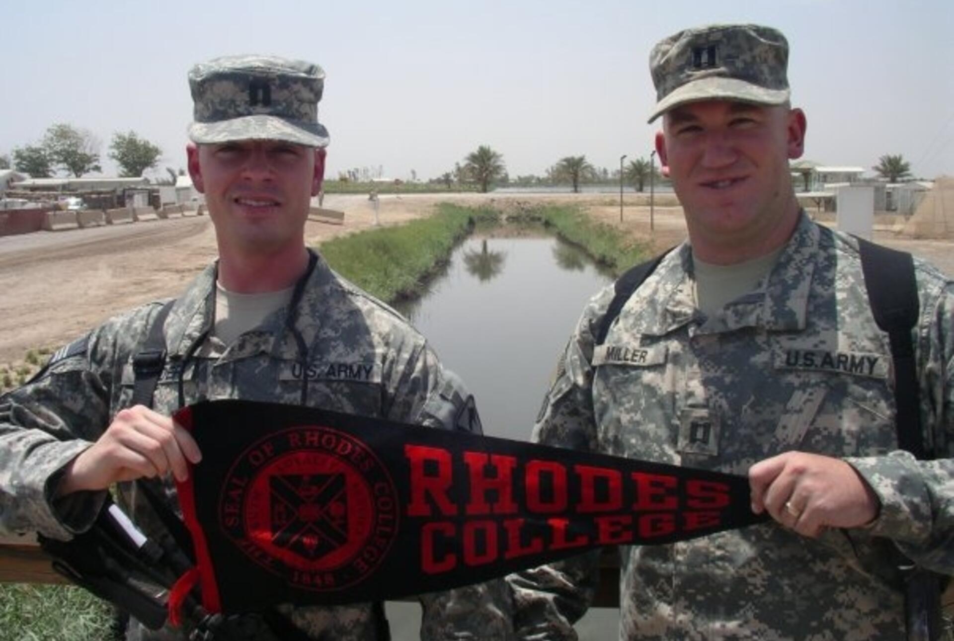 Two male students in US Army fatigues hold a Rhodes College Banner