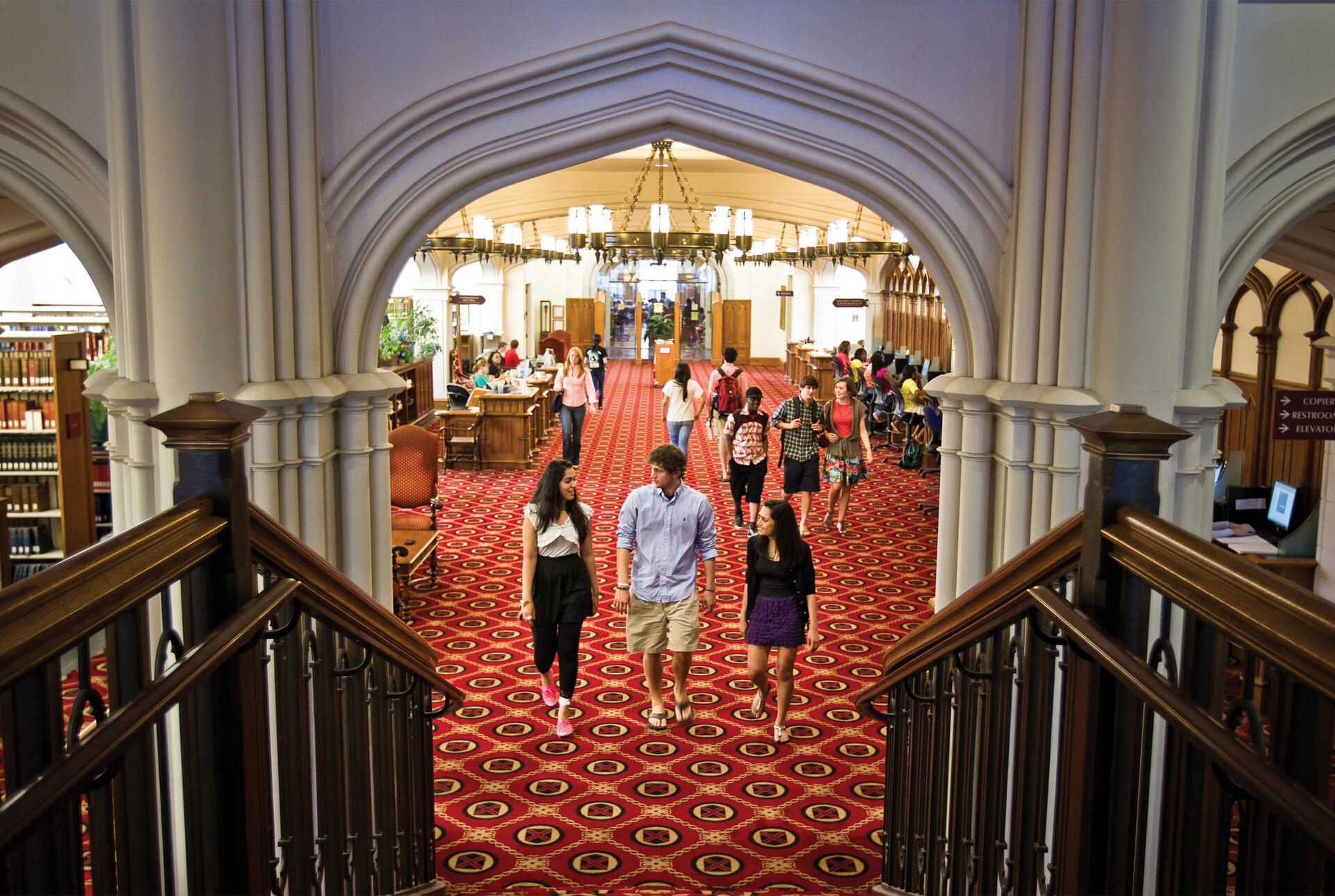 Three students approach the stairs on the main floor of the library