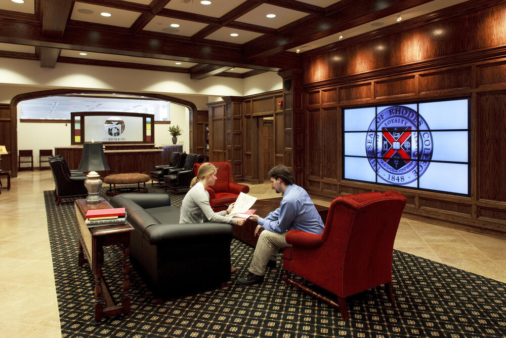 Two people sit in arm chairs in a large room and review financial aid options.