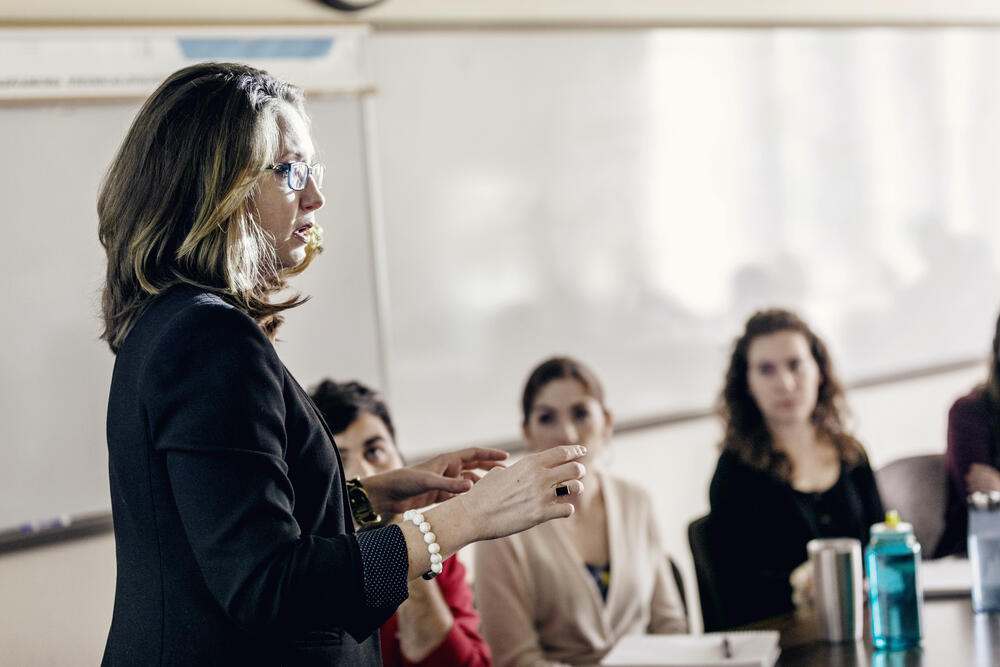 A professor, seen in profile, speaks to her assembled class.