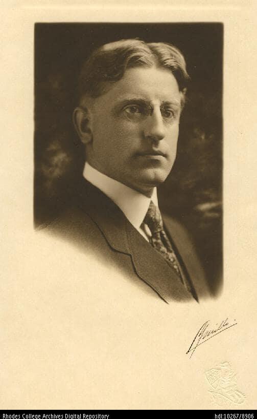 A portrait of a man rocking the middle part in the 20s, wearing a suit and pince nez glasses. 