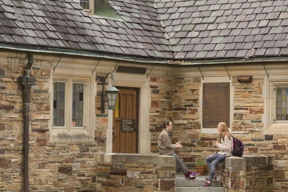 Two girls sitting in front of a sandstone building with a slate roof.