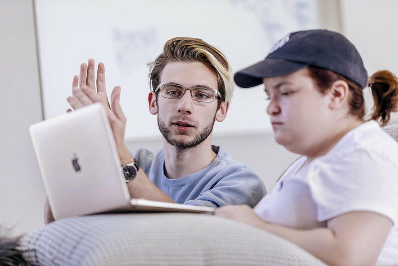 a male student helps another student on a laptop