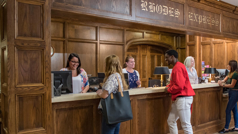 students doing business at a counter with oak paneling in the background.