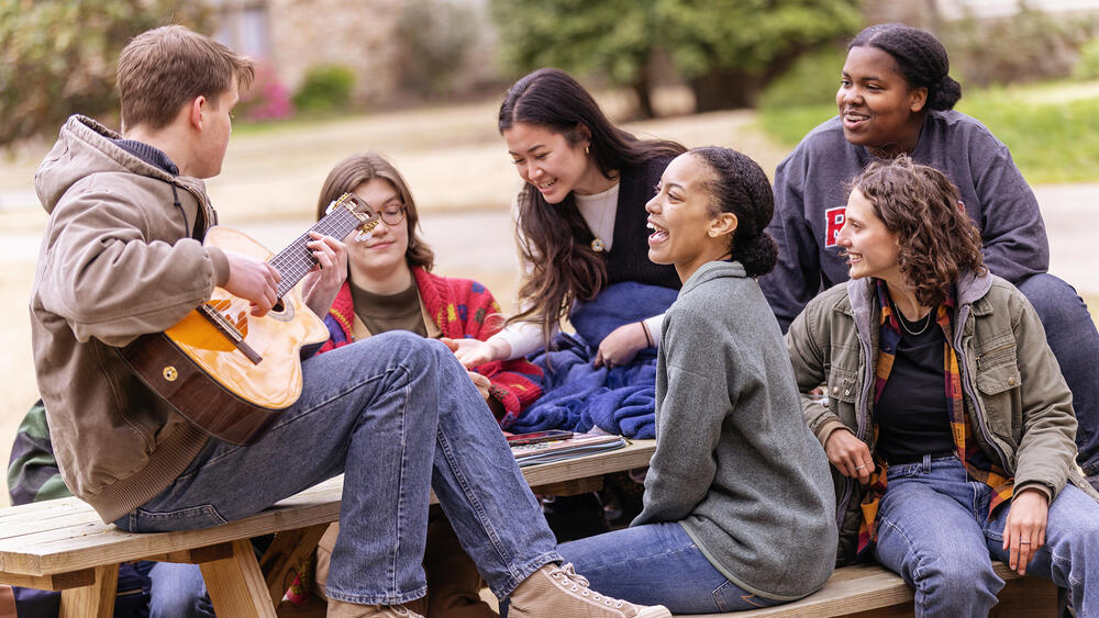  a male student plays guitar for a group of students