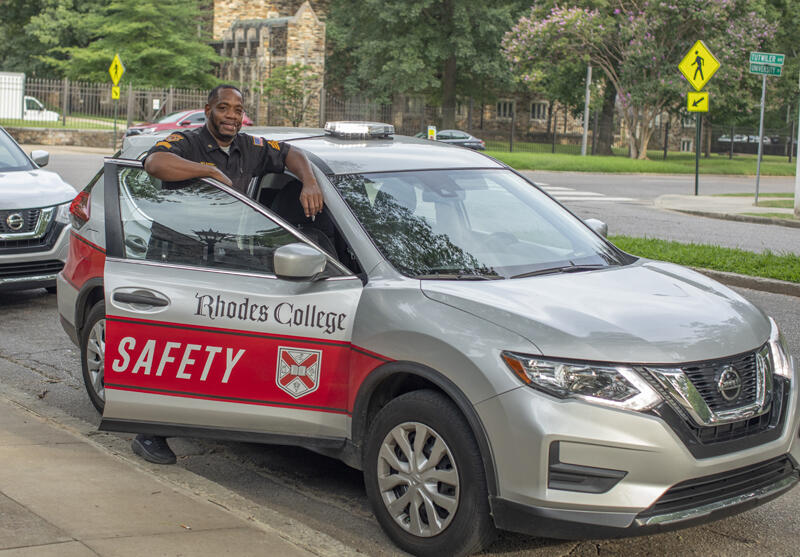 a smiling officer stands next to a campus safety car