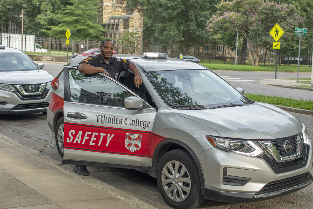 A campus safety officer leaning on their car.