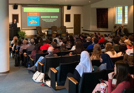 students seated in an auditorium listen to a panel discussion on a stage