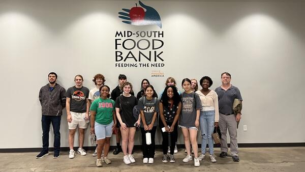 a group of students pose below a sign saying Food Bank