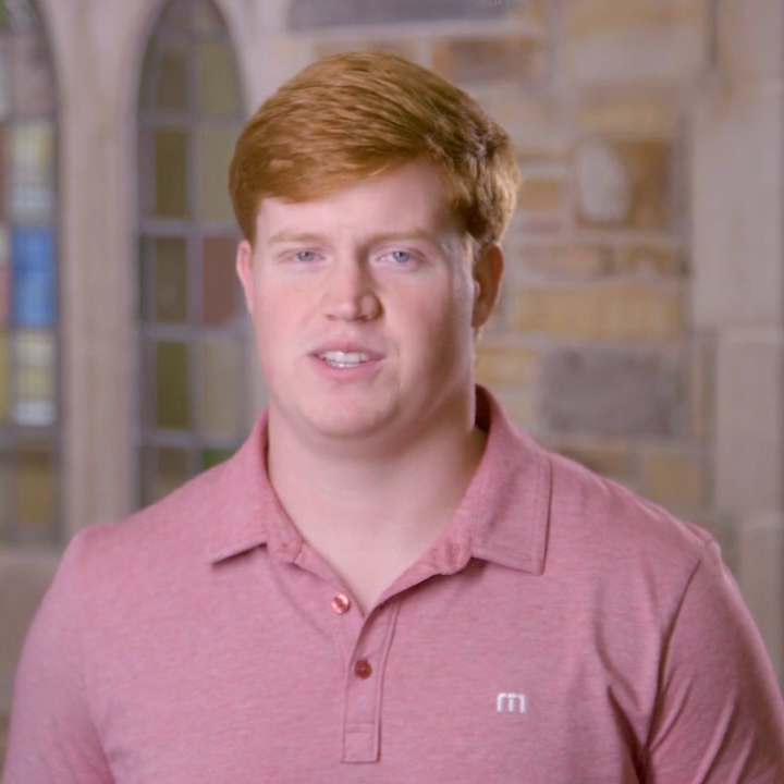 a young man with red hair wearing a salmon colored polo shirt.