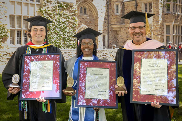 three people in graduation robes hold plaques