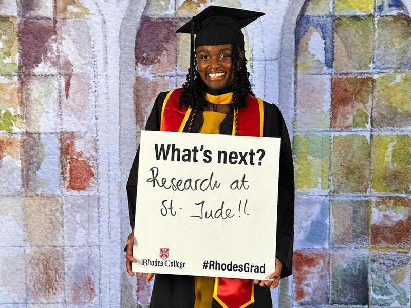 a student in graduation garb holds a sign saying Research at St. Jude