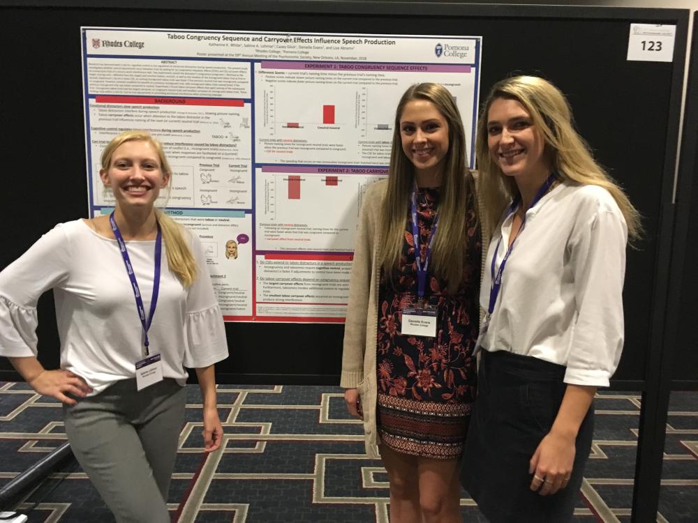 three young women stand next to a poster