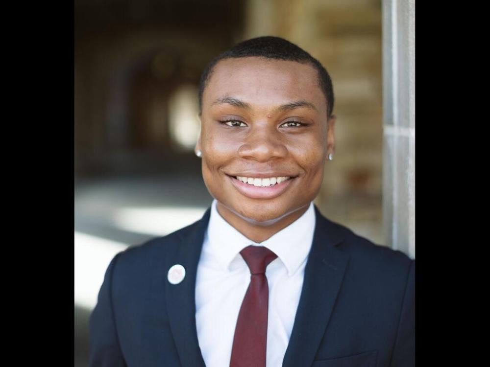 a young Black man in a suit and tie smiles at the camera