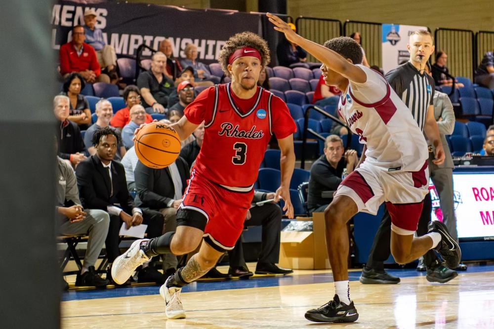 a Rhodes basketball player dribbles the ball past the opposing team