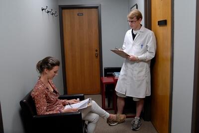 Male student in lab coat interviewing a research participant 