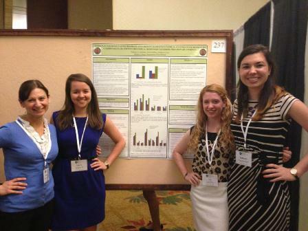 Professor with three female students presenting research on a poster board