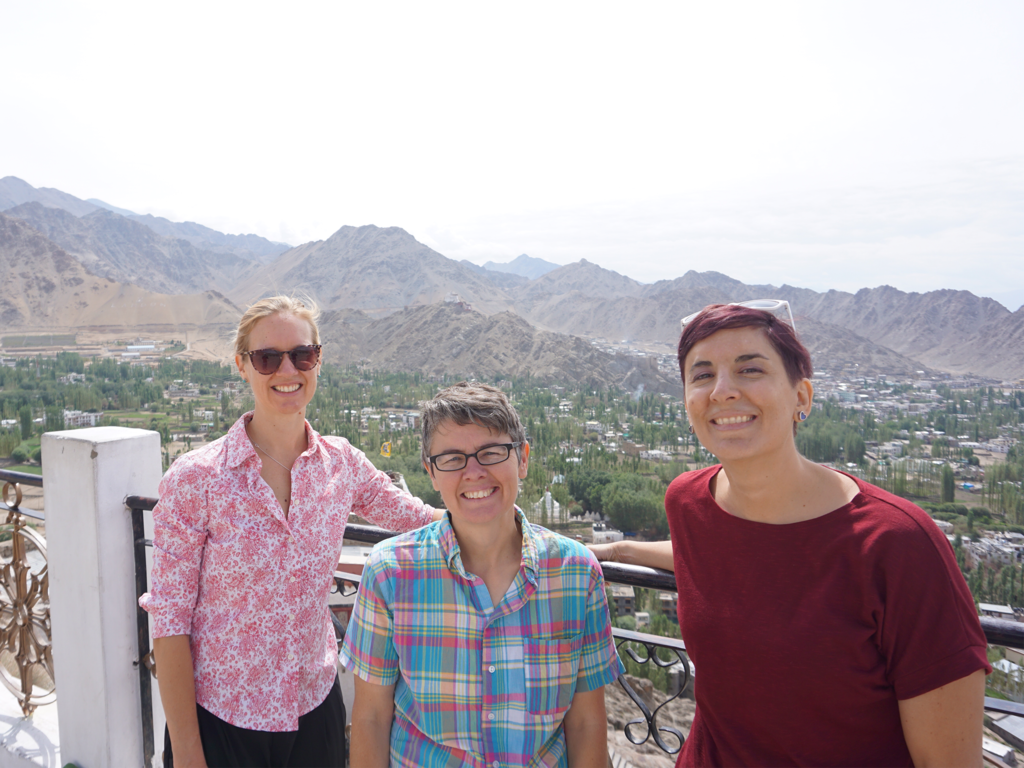 3 female professors standing at a railing looking over a city with mountains in the background.