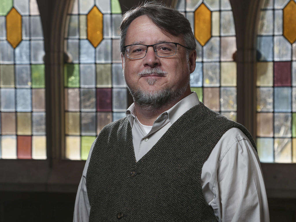 head and shoulder image of a college professor in front of a stained glass window