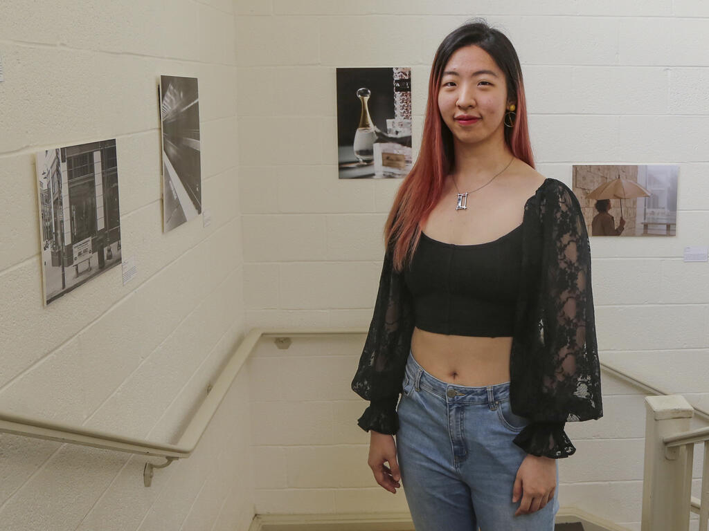 a Chinese woman stands in a stairwell with a photo exhibit