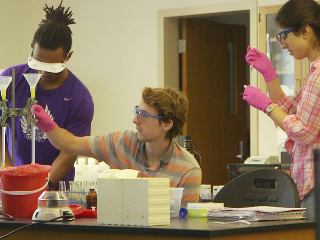 three students measuring liquids in a biology lab containing funnel holders and test tubes