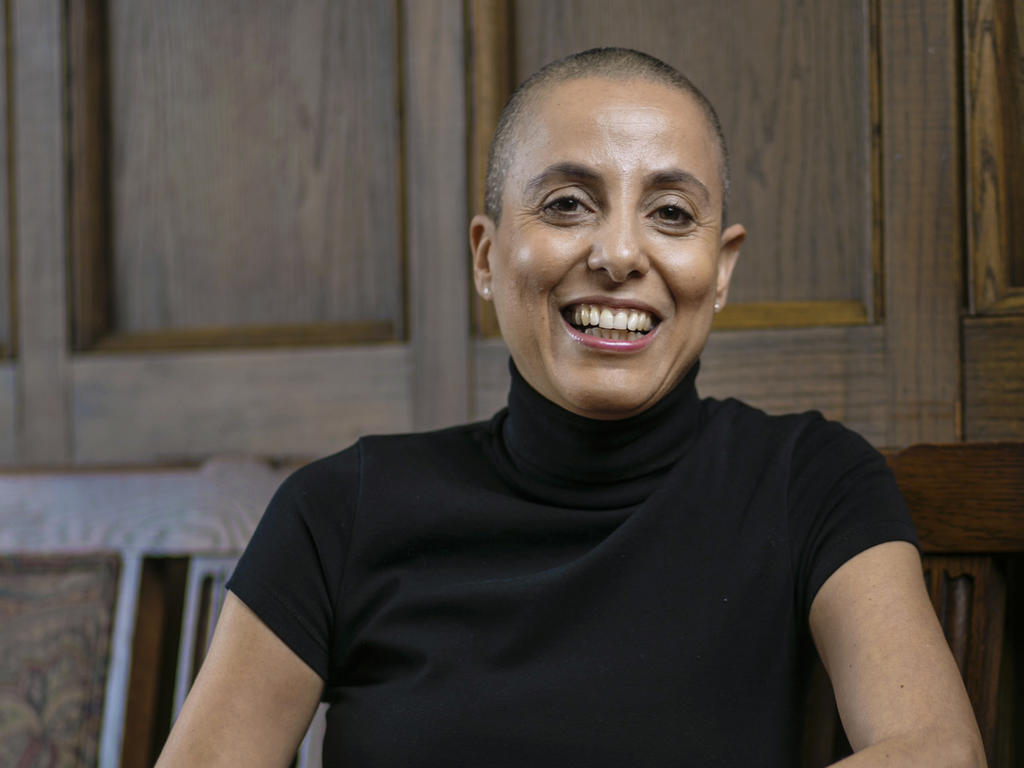 A middle-aged female professor with a shaved head, smiling at the camera