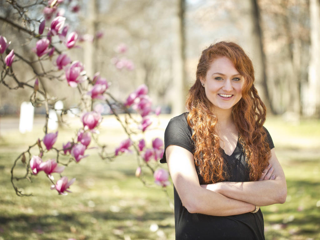 a young red-haired woman smiling near a blossoming tree