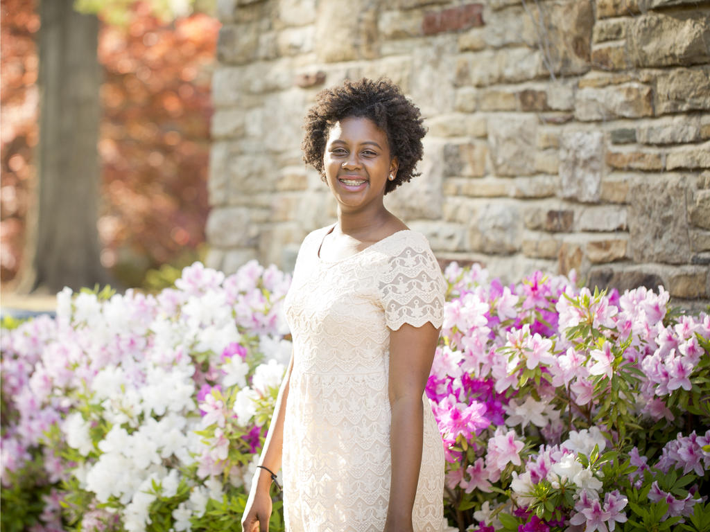an African American female student standing near blossoming flowers 