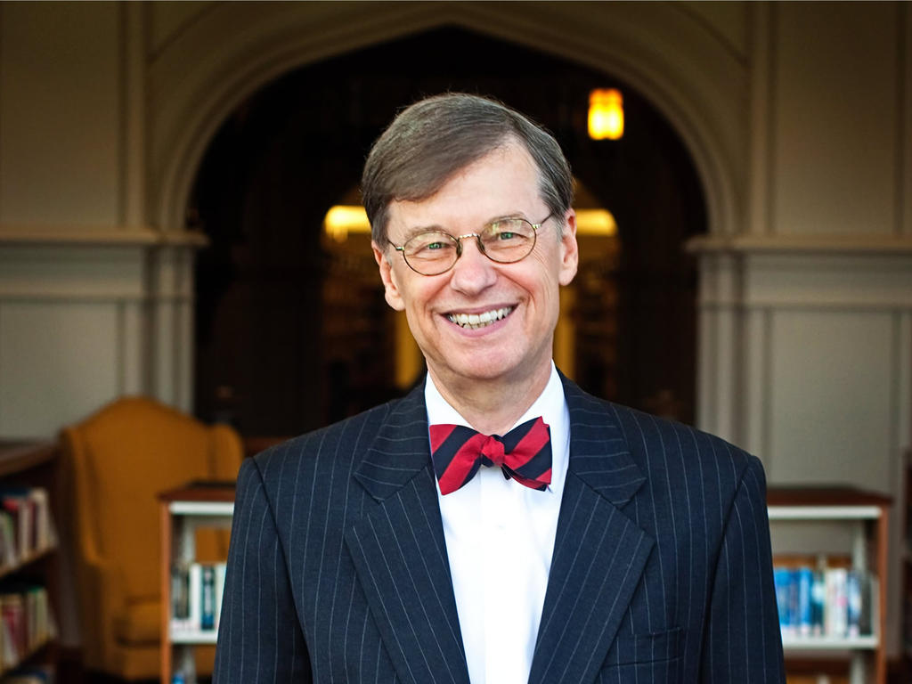 an older male wearing a red bow tie and smiling in the middle of the library