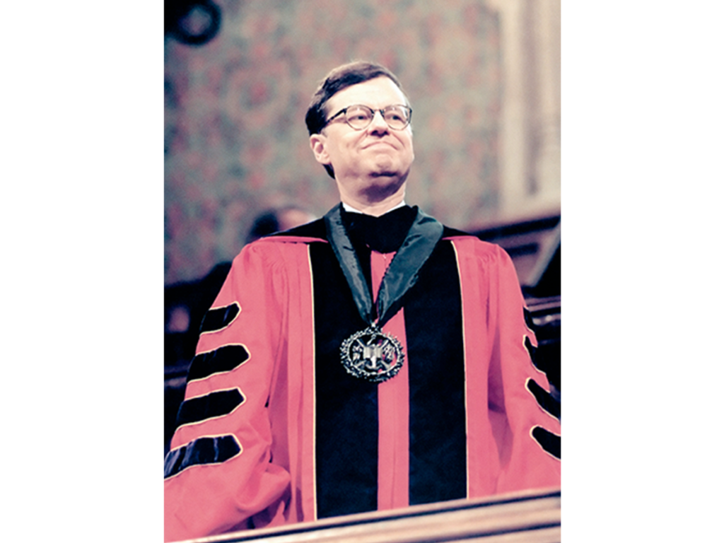 an older white male in academic robing standing wearing a medal to honor him