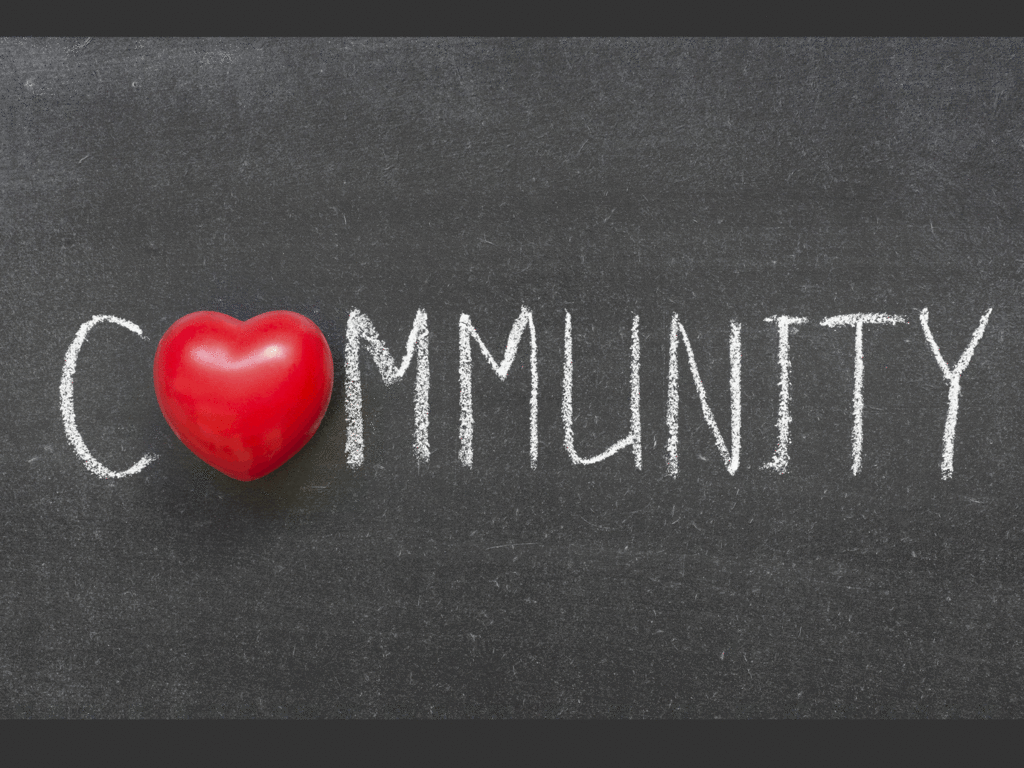 the word "community" written out on a chalkboard with a cartoon heart replacing the letter "o"