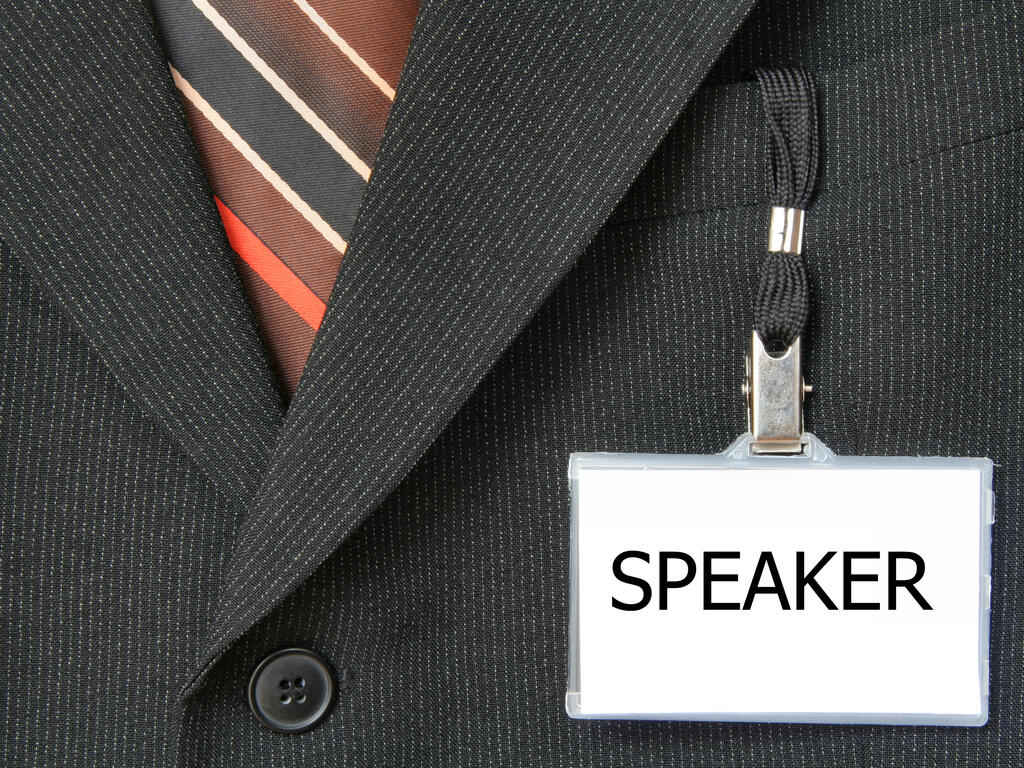 a closeup of a tie tucked into a suit jacket with a name tag that says "Speaker" hanging from the collar