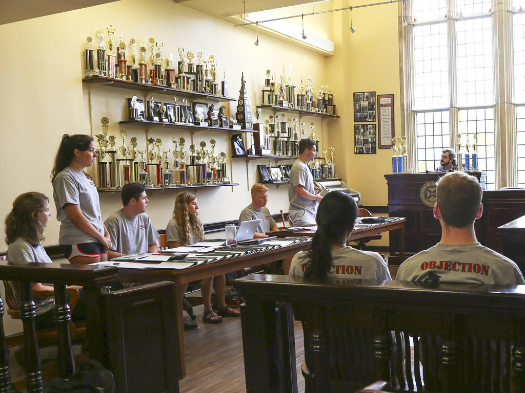 students sitting in a mock court room with trophies lining one wall