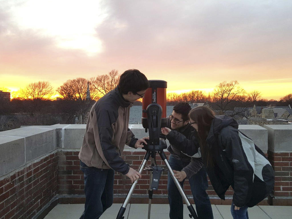 physics students handling and setting up a telescope at sunset 